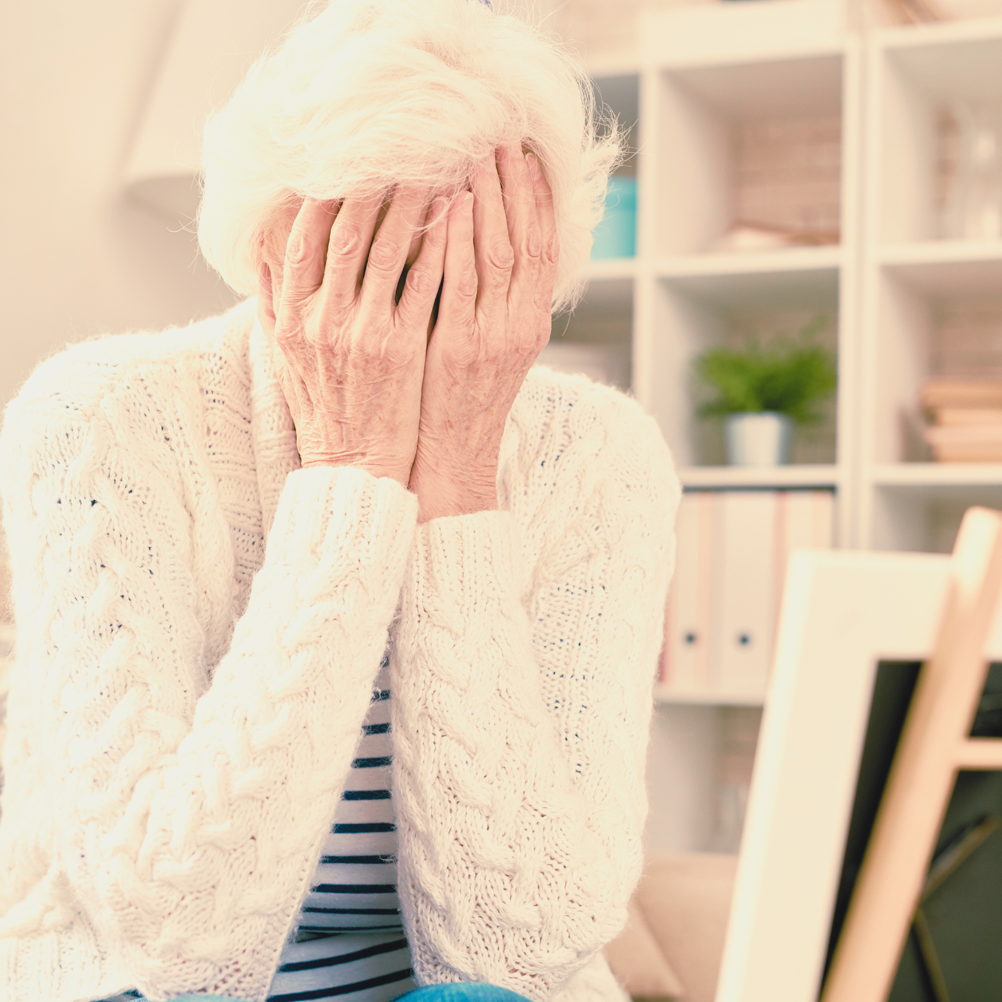 An elderly woman covering her face with her hands, appearing distressed and overwhelmed.